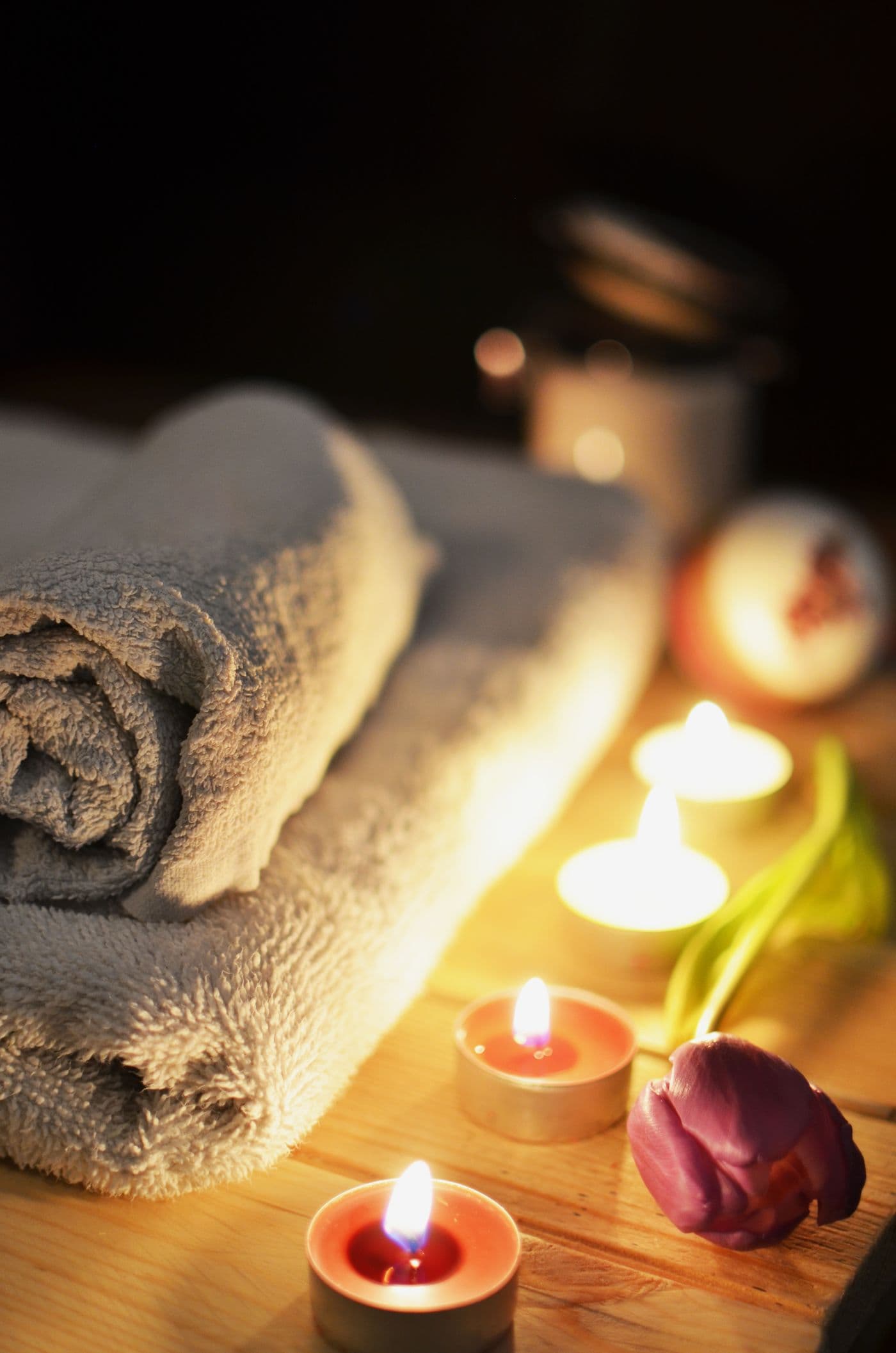 A rolled towel beside warm tea lights on a wooden surface